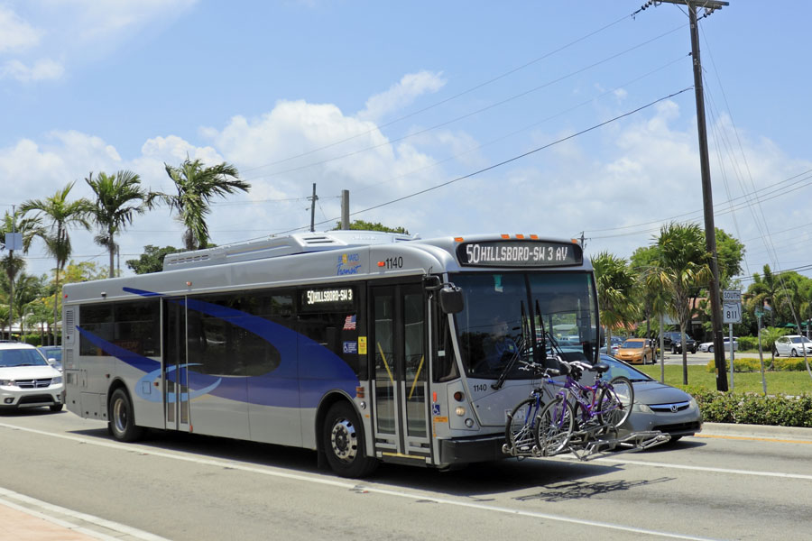 Blue and gray silver public transportation with two bicycles securely stored on the front of the bus as it travels through the sunny day city on Wilton Drive. Wilton Manors, Florida