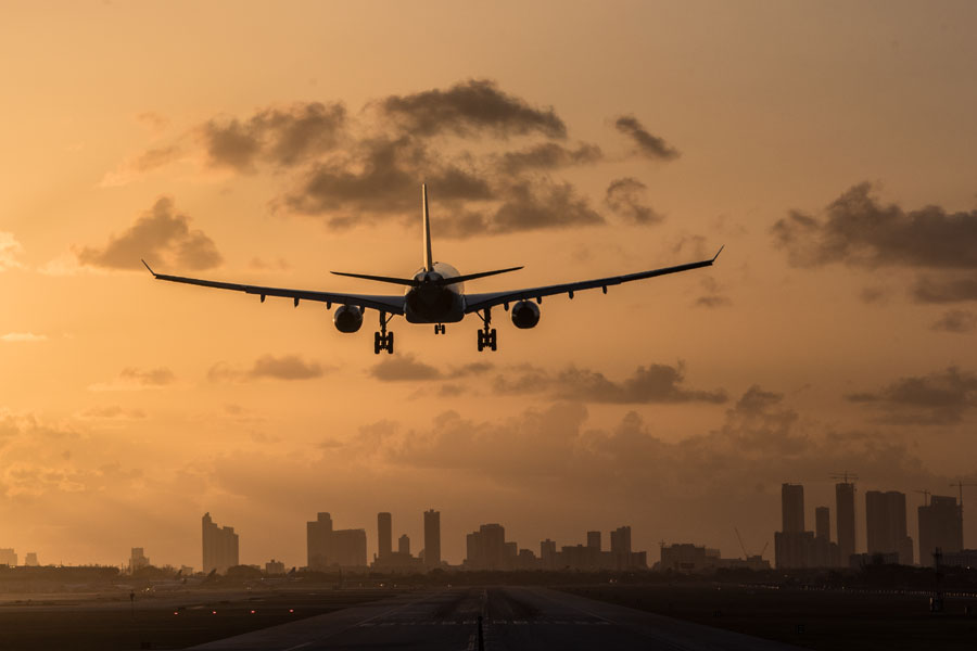 Airplane landing at Miami International Airport at sunrise with Miami Downtown skyline in the background.