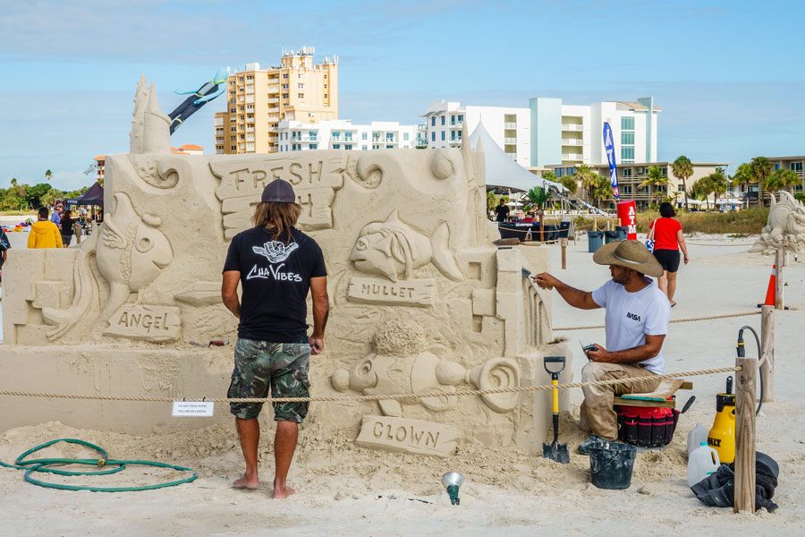 Two sculptors work on a piscatorial creation at a sand sculpting exhibition and competition on a sandy island beach in view of hotels along a Treasure Island beach in Pinellas County, Florida.